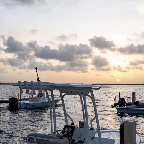 Boats docked by a pier at sunset, with a cloudy sky and calm water in the background.