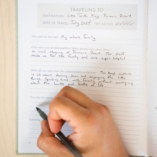 A person is writing in a journal. The entry includes travel details and personal notes.