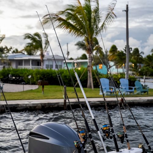 A docked boat with multiple fishing rods, a Yamaha motor, palm trees, and chairs in the background at a waterfront location.