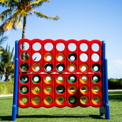 A giant Connect Four game set up outdoors on a grassy area with a palm tree and clear blue sky in the background.