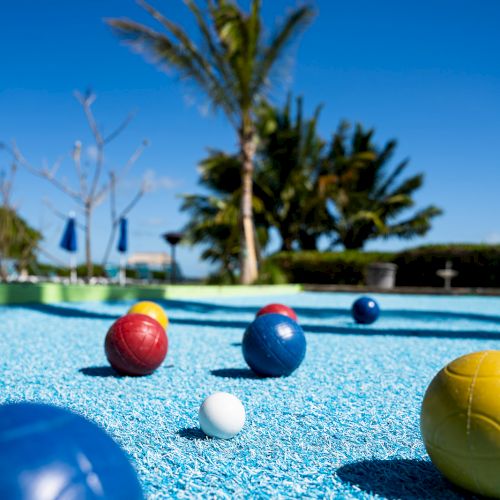 Colorful bocce balls on a textured blue surface with a palm tree and blue sky in the background, creating a vibrant outdoor scene.