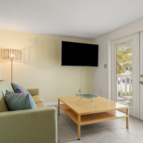 A cozy living room with a green sofa, wooden coffee table, TV, and glass doors leading outside.