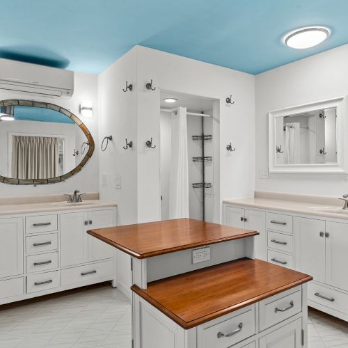 A modern bathroom with white cabinets, two mirrors, wood countertops, and a blue ceiling with two sinks and ample storage space.