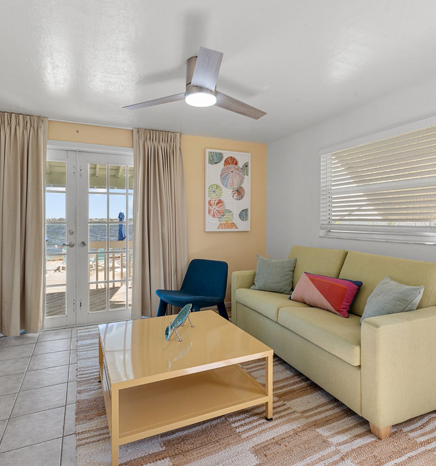 A cozy living room with a green sofa, coffee table, TV, and balcony view. There's modern decor and a ceiling fan.