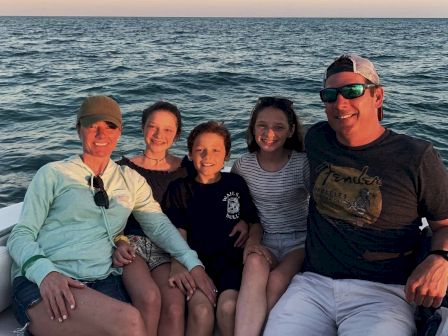 A family of five is sitting together on a boat with the ocean and a sunset in the background.