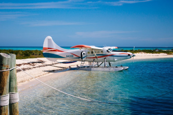 A seaplane is parked on a sandy beach with clear blue water, under a bright sky.